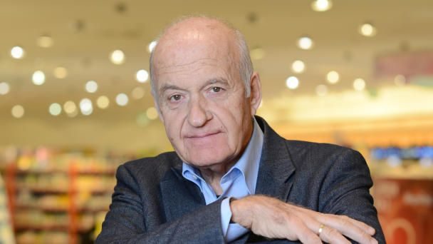 Retail founder Götz Werner sitting in a supermarket aisle